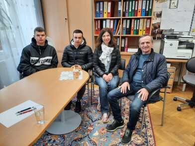 Zwei junge männliche ukrainische Studierenden sitzen neben der Mittelschuldirektorin und deren Koordinator und lächeln etwas zurückhaltend in die Kamera