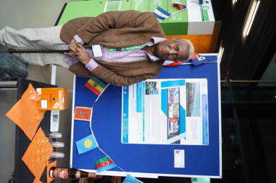 A man with a walking stick stands in front of a poster about his university in Cuba.
