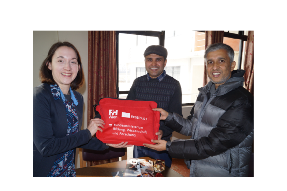 Drei Personen stehen gemeinsam in einem Raum und halten eine rote Tasche. Die Szene zeigt einen symbolischen Moment des internationalen Austauschs im Rahmen einer Lehrendenmobilität in Nepal.